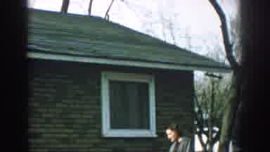 Wisconsin USA (1957): A Woman Stands Near A Brick House As The Side And Windows