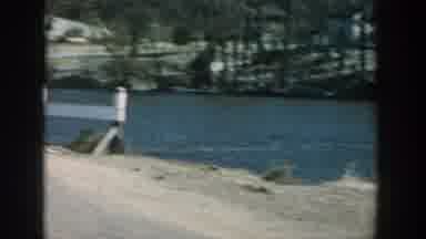 Wisconsin USA (1957): Old Man Fishing On The River Bank Next To A Bridge On A Dirt
