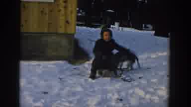 Wisconsin USA (1957): A Boy Sits On His Snow Sled In The Snow And Pets His Dog