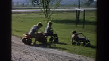 Michigan USA (1958): Three Children Riding In Wagons On Park Grass In Daylight