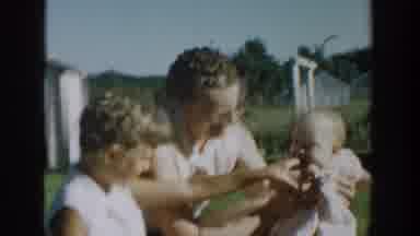 Michigan USA (1958): A Woman And A Girl Play With A Baby On A Grassy Lawn On A