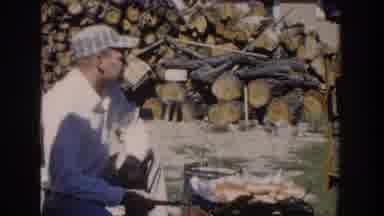 Wisconsin USA (1958): Man Rubs Nose While Cooking Food On Outdoor Grill In