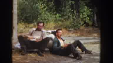 California USA (1936): Two Men Sitting On The Ground Eat Food In The Wilderness