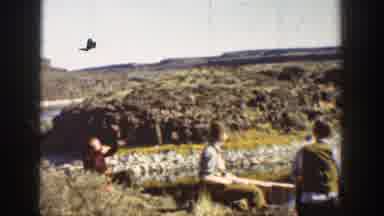 California USA (1936): Men Sitting On Top Of Edge Near River Shooting Shotguns