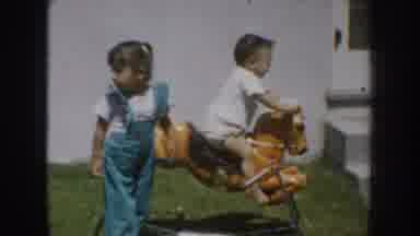California USA (1952): Small Boy Riding A Rocking Horse While Older Girl Stands By