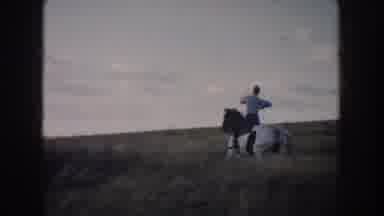 South Dakota USA (1953): Man Riding Black And White Horse Through Field On A Sunny