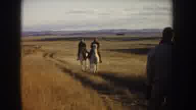 Idaho USA (1955): Two Individuals Riding White Horses Through Countryside Dirt