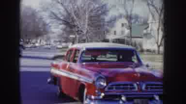 Idaho USA (1955): View Of Person Driving Red Car Down Street On A Sunny Day