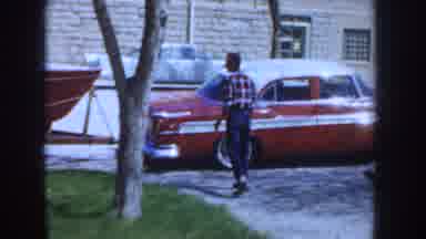 Idaho USA (1955): A Man Walks To His Red Car Parked On The Road Which Is Attached