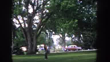 Idaho USA (1955): Vintage Car Driving Past Man Throwing Ball To Friend In Park