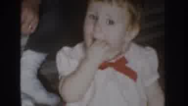 Nebraska USA (1955): Baby Wearing White Dress Sits On Floor Eating