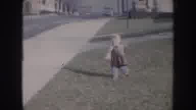 Nebraska USA (1957): Child Runs Across Grass And Sidewalk By The Street In