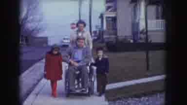 Nebraska USA (1957): A Man Is Disability On The Wheelchair, His Wife Is Pushing