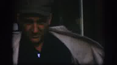 Kansas USA (1958): Man Wearing Green Hat Shows Off Tan Jacket In Front Of Store