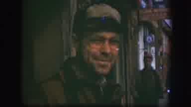Kansas USA (1958): Man Smirking And Squinting Wearing Hat And Glasses Near Men In