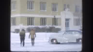 Kansas USA (1958): Two People Walking Towards Tan Building On A Snowy Day