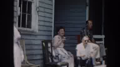 Nebraska USA (1958): Family Gathered On Porch With Old Men Pacing On A Sunny Day