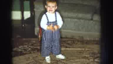 Nebraska USA (1959): Baby Wearing Blue Overalls Walling On White Rug In Front Of