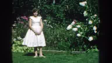 Nebraska USA (1959): Woman In White Dress Standing In The Garden Surrounded By