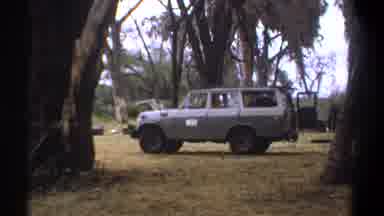 Kenya (1969): Older Grey Suv Parked Near A Man Doing Laundry Outdoors