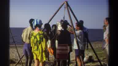 Nigeria (1969): Group Of People Hangs A Large Caught Fish From A Tripod On A Beach