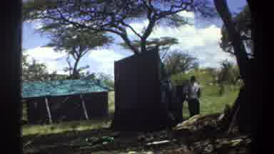 Lagos Nigeria (1969): Men Carrying 2 By 4 Planks Towards Outdoor Shed On A Sunny