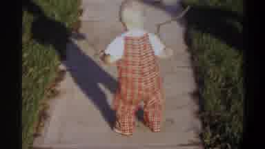 Gainsville Florida USA (1974): Baby Wearing Red Overalls Picks Up Stick Woman