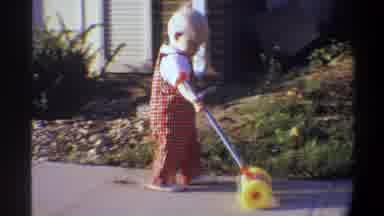 Gainsville Florida USA (1974): A Toddler Walks On A Sidewalk Pushing Their Toy