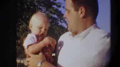 Gainsville Florida USA (1974): Man Wearing White Shirt Holds Baby Wearing Red