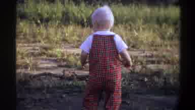 Gainsville Florida USA (1974): Baby Wearing Red Overalls Looking Down Man Picks Up