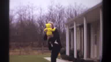 Gainsville Florida USA (1974): Man Wearing Black Suit Walking Holding Baby Wearing
