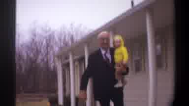 Gainsville Florida USA (1974): Man Wearing Black Suit Walking Holding Baby Wearing