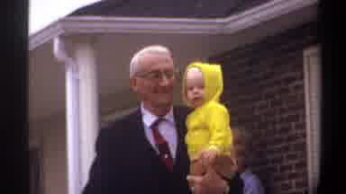 Gainsville Florida USA (1974): An Elderly Man Holds A Baby In Front Of A Brick