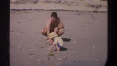 Gainsville Florida USA (1974): Man Plays With A Child In A Yellow Hat In The Sand
