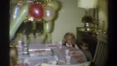 Gainsville Florida USA (1974): Girl Wearing Blue Picks Up Little Boy At Table