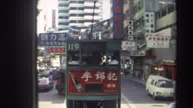 Hong Kong (1982): Double Decker Rail Car And Other Traffic Drive Within A Busy