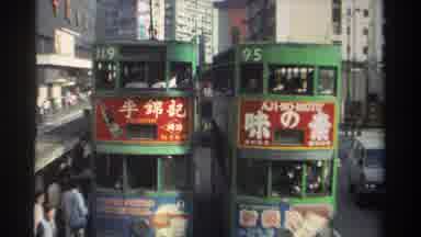Hong Kong-1982: Double Deck Tram Cars Move Down An Urban City Street In The
