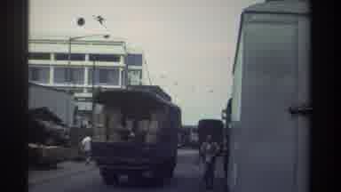 Hong Kong (1982): Train Driving Through City People Walking On Street Past Trucks