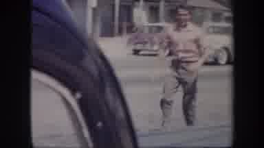 Arizona USA-1957: Man Waving on Street as Classic Cars Pass by Near Ghost Town Sign