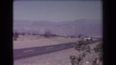 Arizona USA (1958): Man Wearing Brown Pants Walks Past Yellow Brown Car On Bright