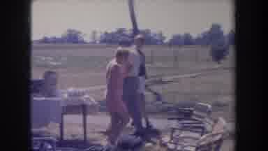 Michigan USA (1968): Woman Dressed In Pink Walking Through A Picnic And Talking To