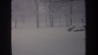 Michigan USA (1968): Older Car Driving In Snow Pan To Right Showing Snowy