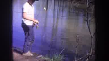Michigan USA (1968): Boy Stands Near Body Of Water And Baits Fishing Pole On Sunny