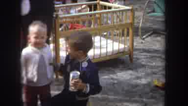 Michigan USA (1968): Boy Holding A Drink Can Shakes The Arm Of A Toddler While He