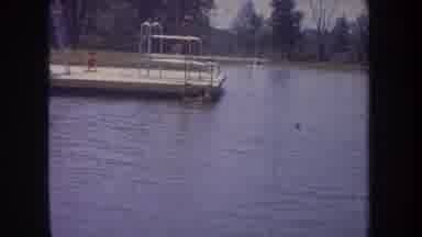 Michigan USA (1968): Person Diving Into Water While Someone Climbs Out Of Water On