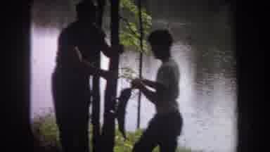 Michigan USA (1968): An Older Man Attempting To Hand A Fish To His Son While In
