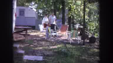 Michigan USA (1968): Man And A Woman Walking Among Folding Chairs In A Forest