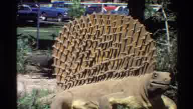 Western USA (1980): Stegosaurus Statue Sits Ina Greenery Area In Front Of A