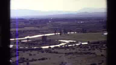 Western USA (1980): Winding River Cutting Through Flat Land With Mountains In The