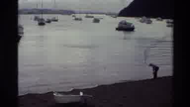 New Zealand (1981): Person Bending Over Near Shoreline With Boats In The Harbor